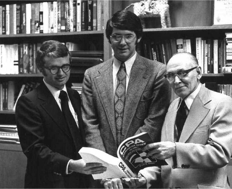 Left to right: (L) Irvin Gleim, (C) Charles McDonald, (R) Lawrence Benninger. All 3 are looking at a printed CPA Book from the 70s.